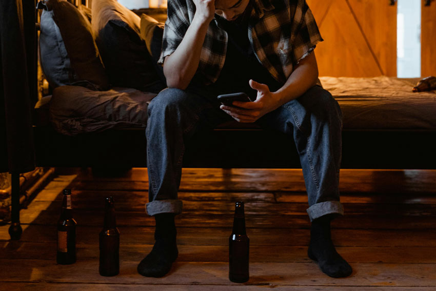 distressed man on his phone with beer bottles scattered around him