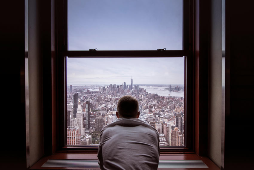 man looking out the window at a city