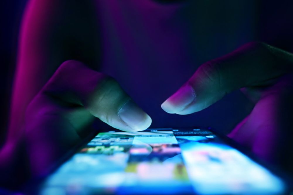 Close-up of hands using a smartphone in low light with a glowing screen, highlighting the use of mobile apps for support or wellness.